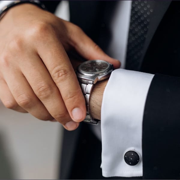 Man in a suit adjusting a stainless steel bracelet watch on his wrist